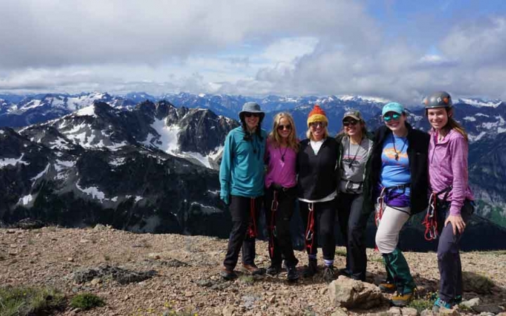 a group of women stand on a summit that overlooks a snowy mountain landscape